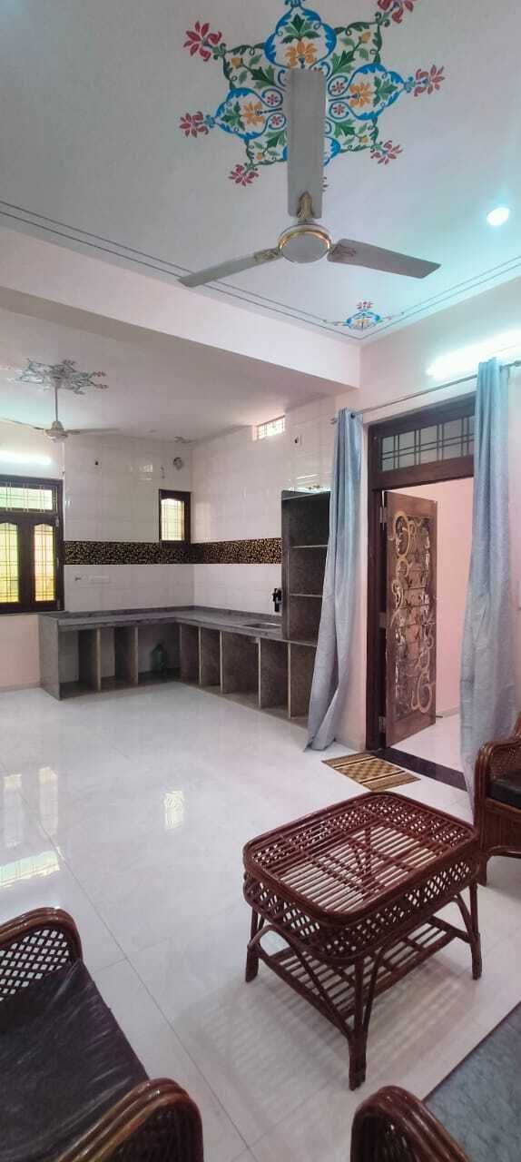 Spacious living room with cane furniture, tiled flooring, ceiling fan, decorative ceiling art, and open kitchen area